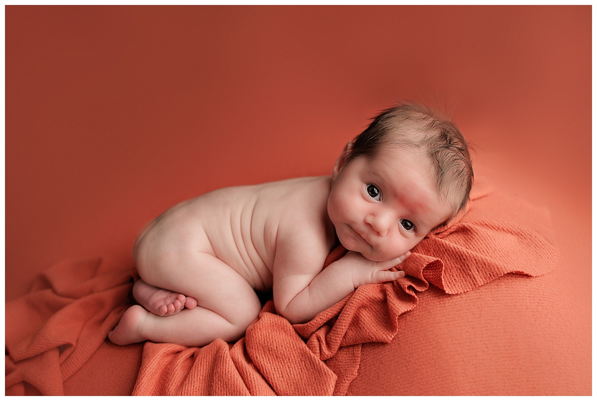 Baby lays on the orange sheet with sweet eyes showing Why Newborn Photography is Worth the Investment