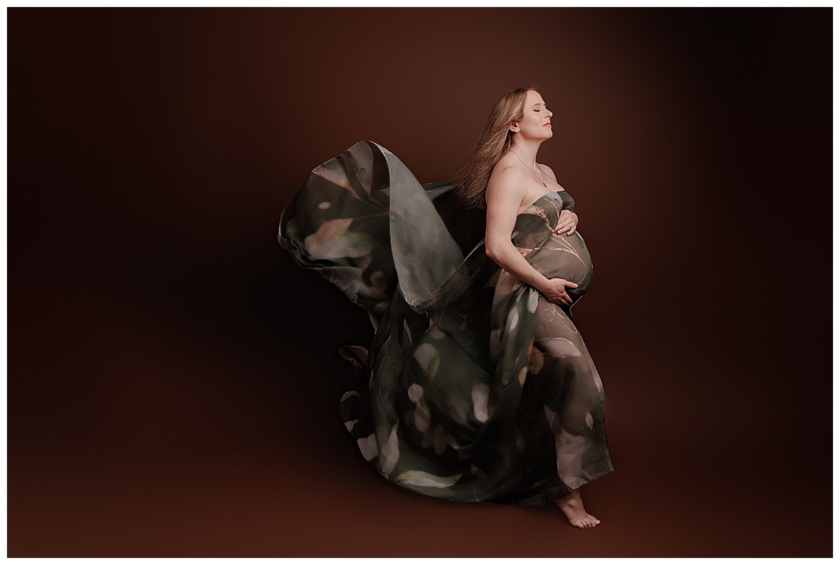 Woman embraces her pregnant belly with gown flowing behind her for Silver Spring Maternity Photographer