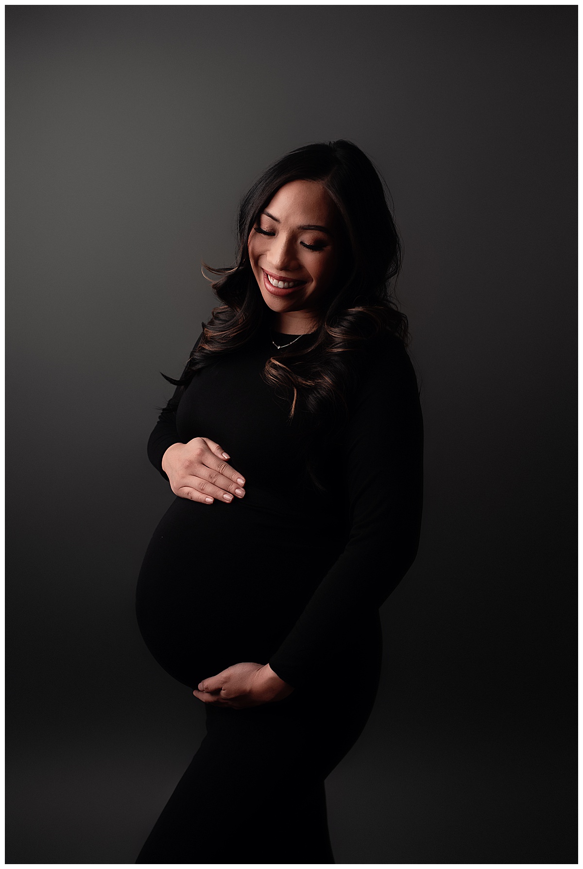 Female holds her hand on her pregnant belly wearing a black gown for Silver Spring Maternity Photographer