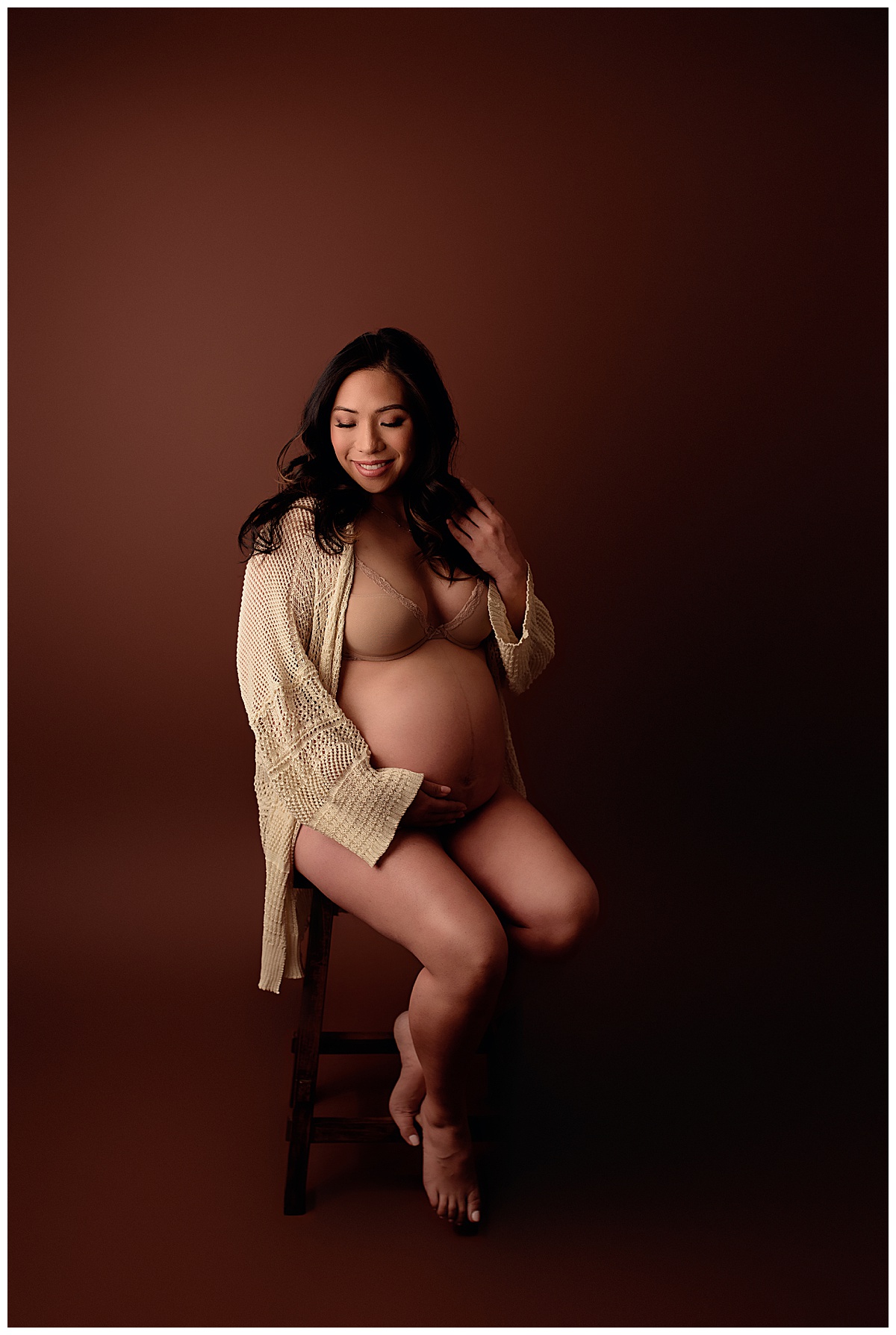 Adult sits on the chair embracing her pregnant belly for Yaffa Koff Photography