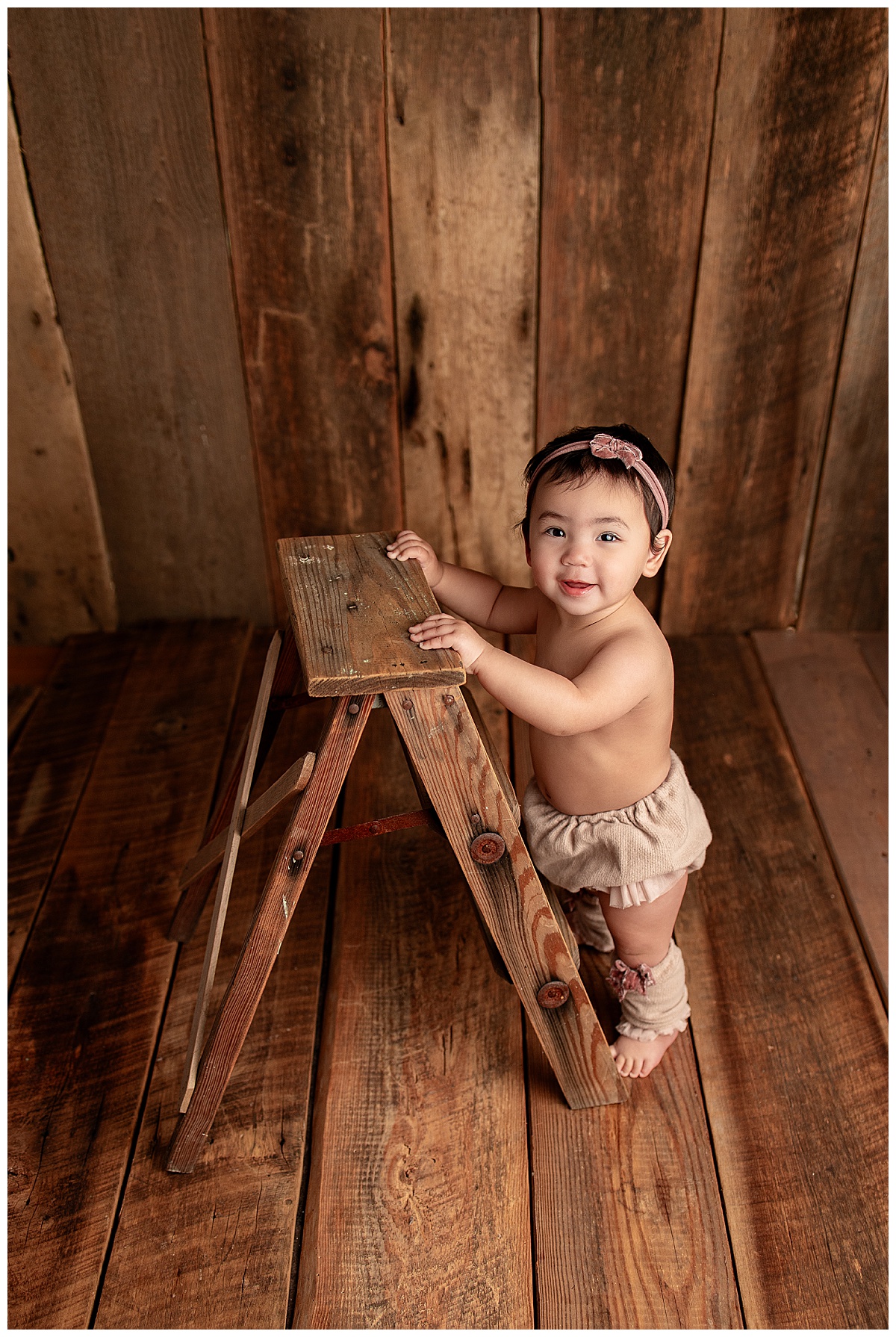 Young baby holds onto a ladder during a set of Milestone Sessions