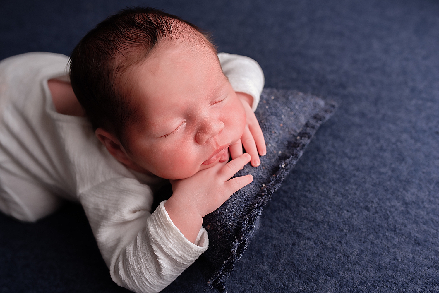 infant lies on blue pillow by Yaffa Koff Photography